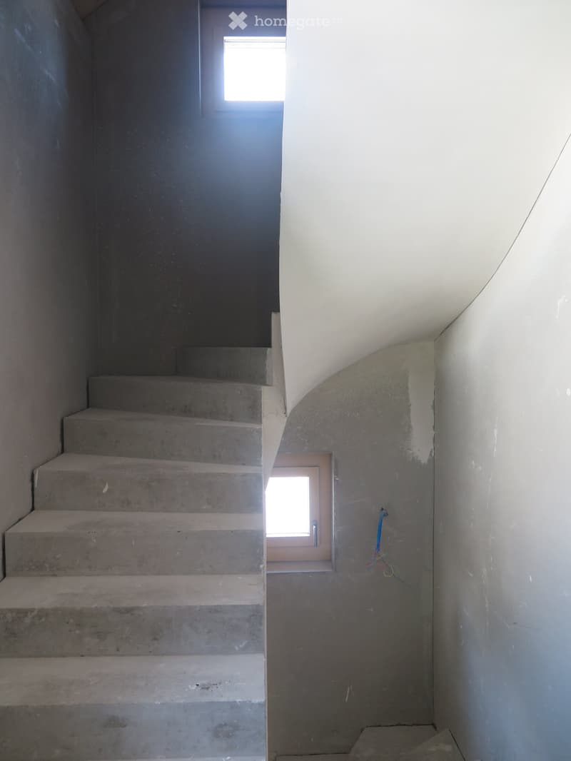 Concrete staircase leading upwards with white walls and small windows on either side, showing unfinished interior with visible construction materials.