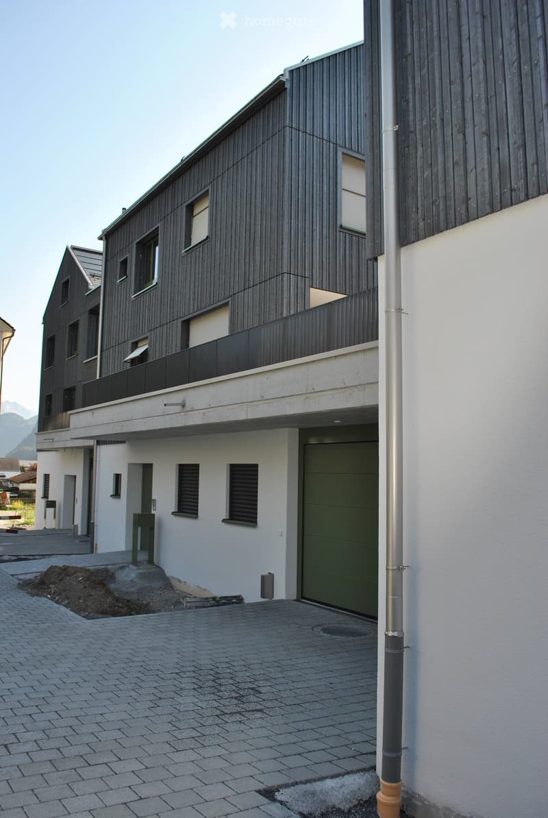 Modern two-story building with dark wooden facade, white lower section, garage, and balcony on the upper level.