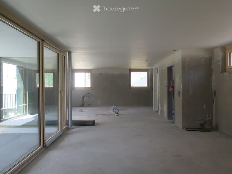 Empty room with bare concrete walls and floor, large glass sliding doors, and small windows allowing natural light.