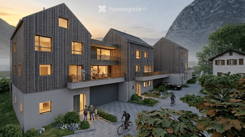 Modern multi-story residential building with wooden facade, large windows, balconies, garage, and parking area, set against a scenic mountain backdrop.