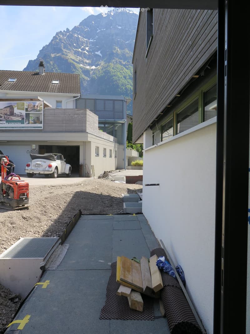 Outdoor area with a view of mountains, a garage with a white convertible inside, and construction materials on the ground.