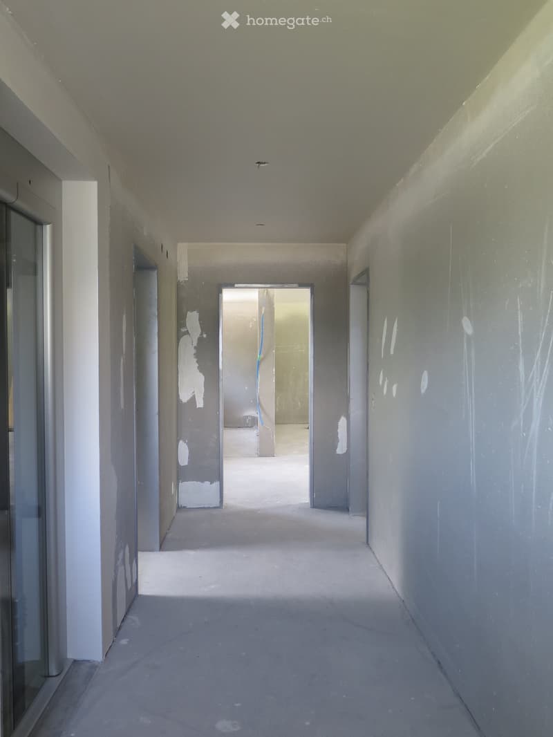 Empty, unfinished hallway with bare concrete floors and walls, featuring several open doorways leading to other rooms.