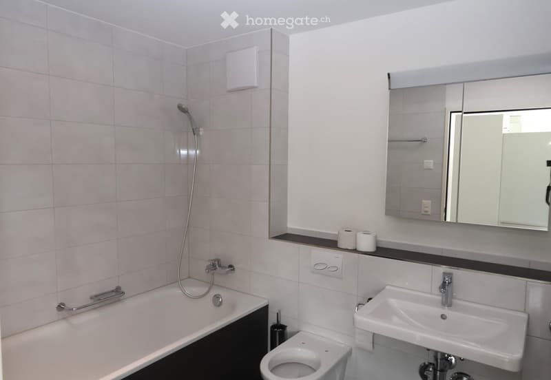 White tiled walls, bathtub, toilet, sink, mirror, power outlets, shelves
