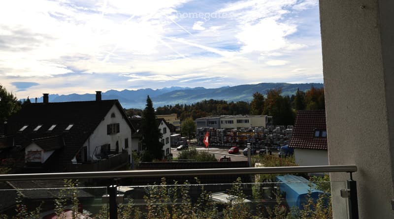 balcony with railing, residential buildings, mountains, vehicles parked, greenery