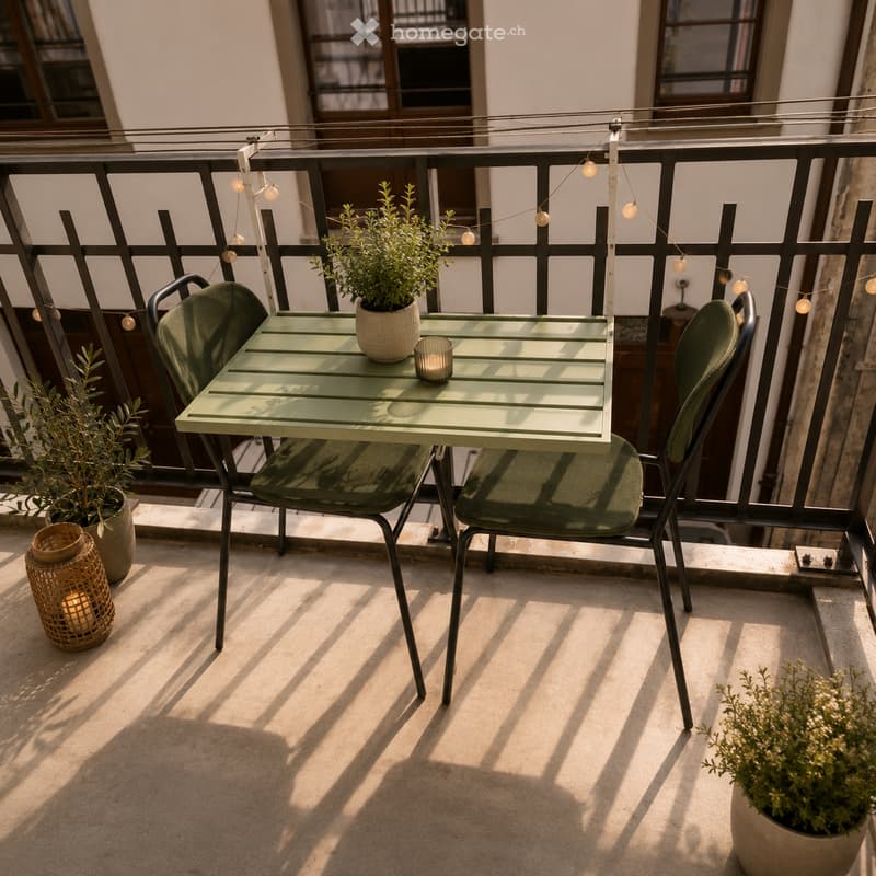 Balcony with a small green table, two matching chairs, potted plants, and string lights.