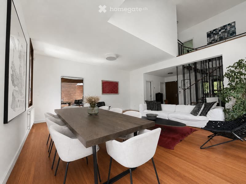 Modern living and dining area with white walls, wooden flooring, a white sofa, a wooden dining table, and chairs.