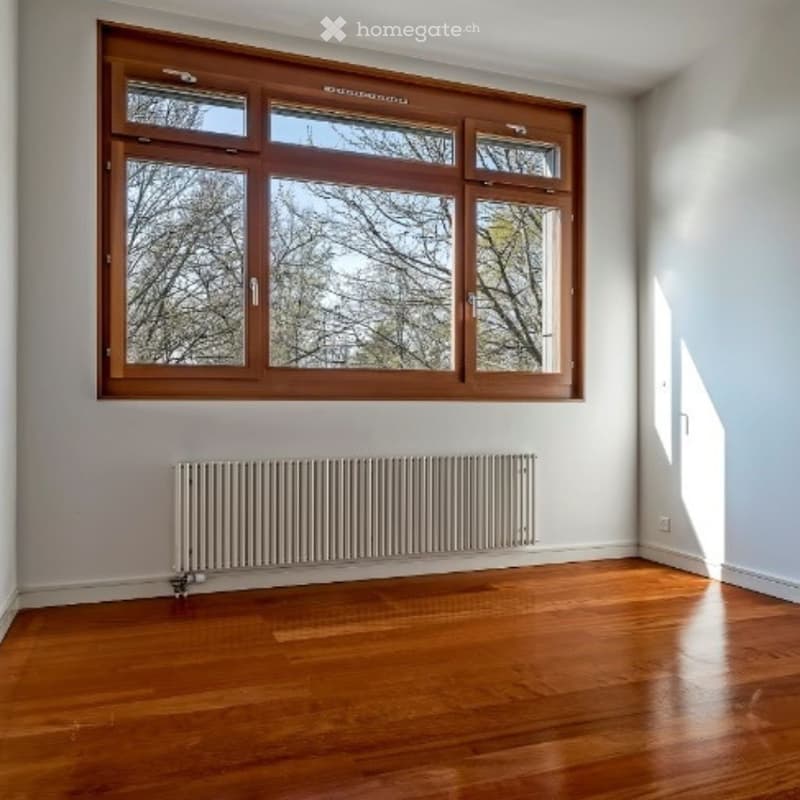 Empty room with wooden flooring, large wooden-framed windows, and a radiator against one wall.