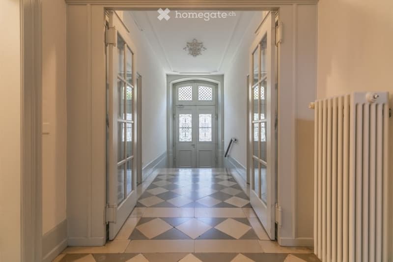 Elegant hallway with checkered tile flooring, double doors at each end, and a chandelier hanging from the ceiling.