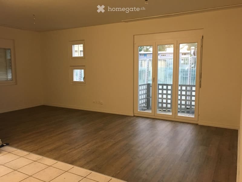 Empty room with wooden flooring, large sliding glass doors leading to a balcony, and small windows on the wall.
