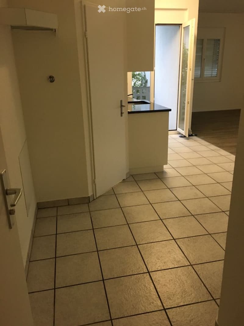 Empty hallway with tiled floor, white walls, and a partially open door leading to another room.