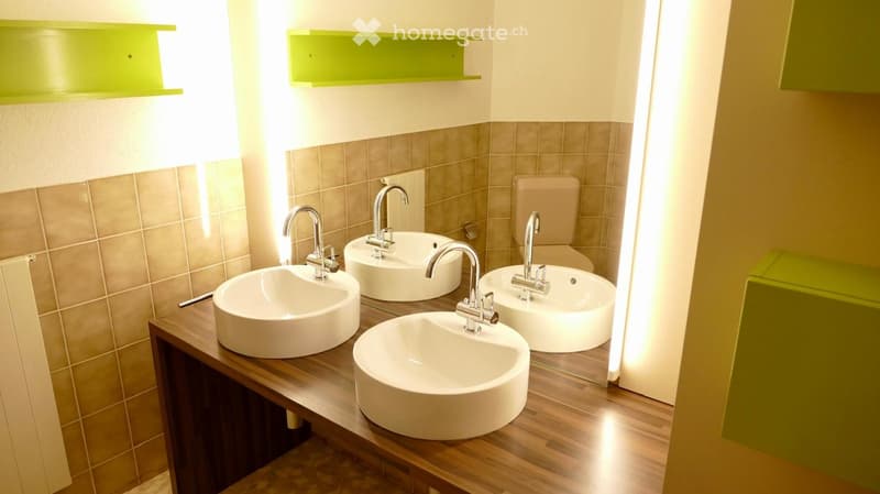 Modern bathroom with four round sinks on a wooden countertop, each with a chrome faucet, and a toilet in the background.