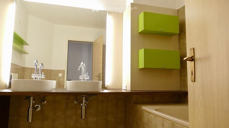 Modern bathroom with two sinks, faucets, a bathtub, and green wall cabinets.