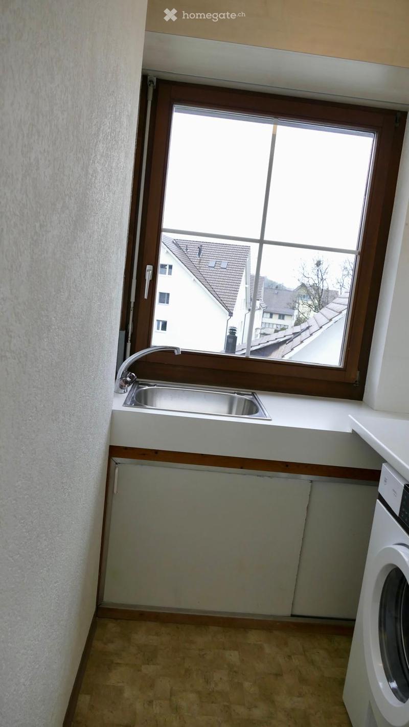 Small bathroom with a window, a sink with a faucet, and a washing machine. The space is clean and well-lit with light-colored tiles and walls.