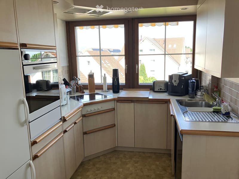 Bright kitchen with light wood cabinets, stainless steel appliances, and a large window overlooking a residential area.