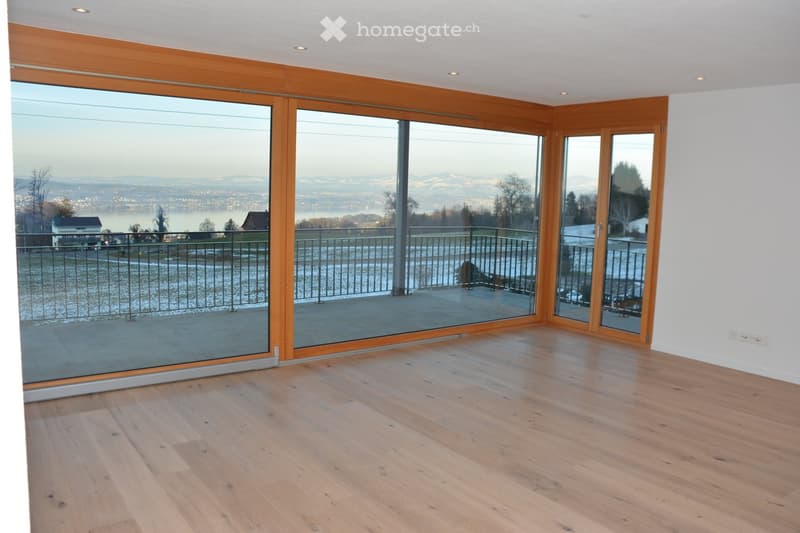 Empty room with wooden flooring and large glass sliding doors leading to a balcony with a scenic mountain view.