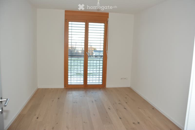 Empty room with light wooden flooring, white walls, and a large wooden door with glass panels leading outside.