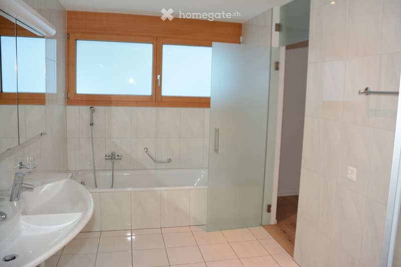 Modern bathroom with a white tiled floor and walls, a large sink with a chrome faucet, a bathtub with a handheld showerhead, a glass shower enclosure, and a large mirror above the sink.