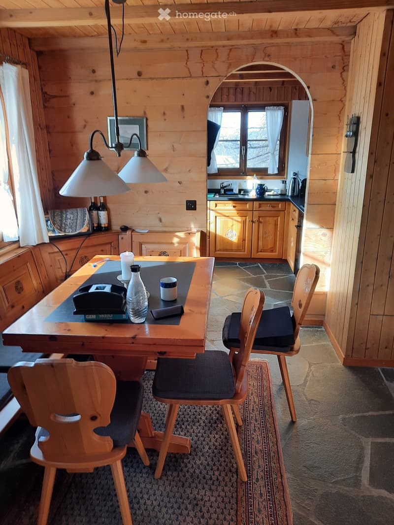 A cozy wooden interior with a dining table, chairs, and a small kitchen area with cabinets and a sink.