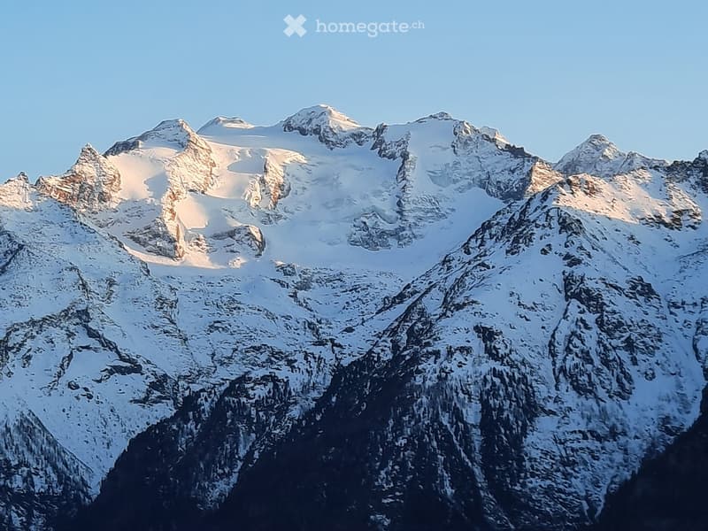 Snow-capped mountain range with rugged peaks and deep valleys, illuminated by sunlight.