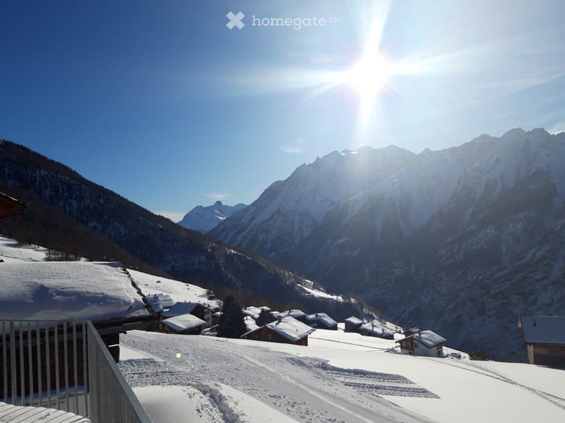 A snowy outdoor area with a view of snow-covered mountains and a small village in the background.