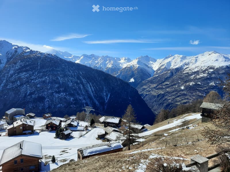 A cluster of houses and buildings in a snowy mountain valley, surrounded by snow-covered peaks and trees.