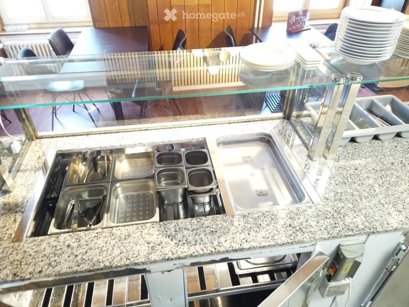 Commercial kitchen with granite countertop, stainless steel sink, multiple bowls, and a glass partition separating the dining area.