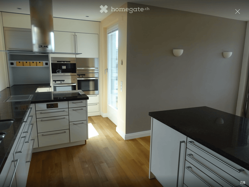 Modern kitchen with white cabinets, stainless steel appliances, black countertops, and wooden flooring.