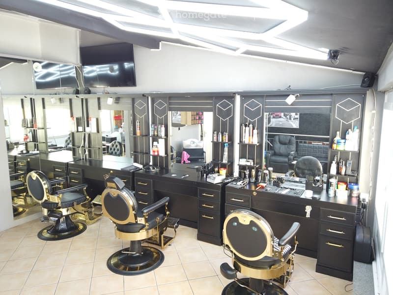 Modern salon with black and gold styling chairs, mirrors, cabinets, and a TV screen.