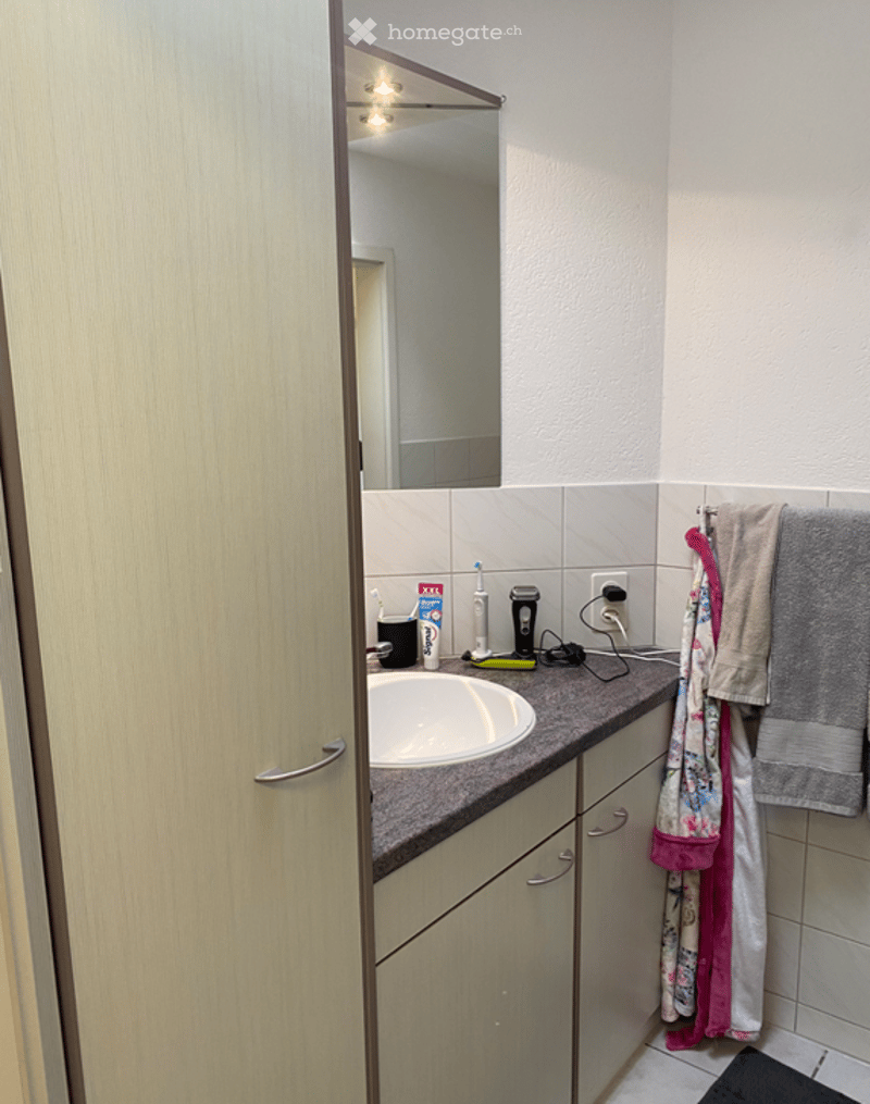 Bathroom with a sink, mirror, and various toiletries on the countertop. Towels are hanging on a rack.