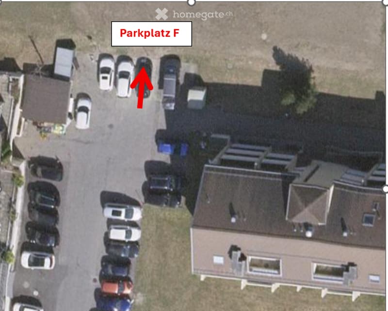 Aerial view of a residential building with a parking lot labeled "Parkplatz F" and several parked cars.