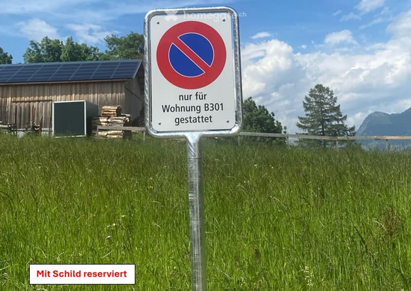 A grassy field with a sign indicating restricted access for residential use, a wooden shed with solar panels, and a stack of logs nearby.