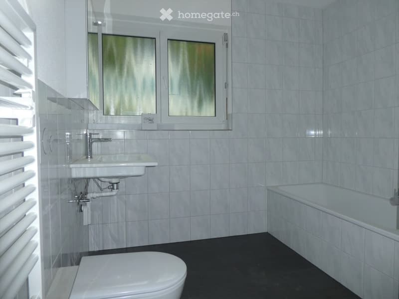 Bathroom. Modern bathroom with white tiles, a sink, a bathtub, and a toilet. The room features a window with frosted glass and white blinds.