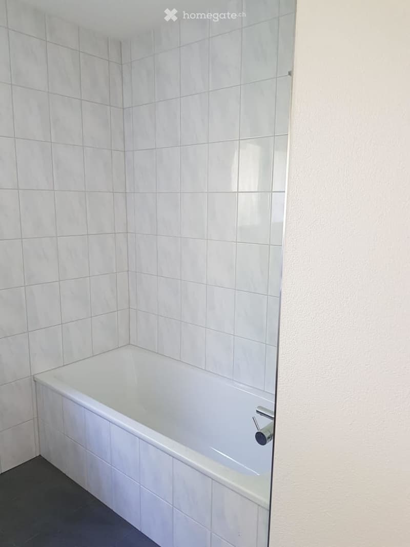 Bathroom. Clean, modern bathroom with white tiled walls and a bathtub. The space features a sleek, contemporary design with a glass shower enclosure visible on one side.