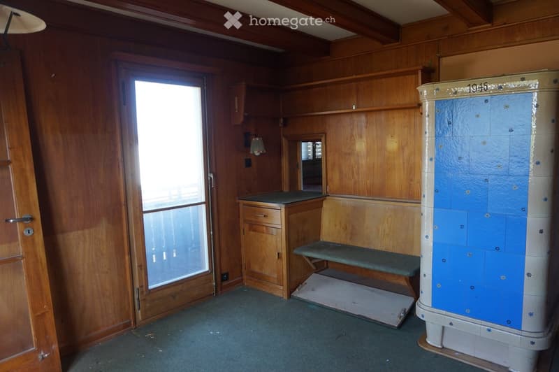 Empty room with wooden walls, a small bench, a cabinet, and a vintage stove. The room has a large window and a door leading to another space.