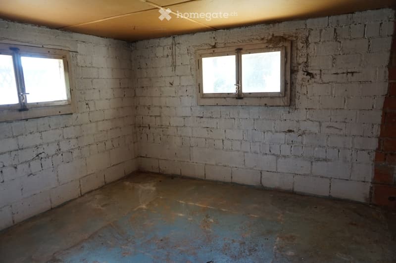 Empty room with exposed brick walls, concrete floor, and two windows allowing natural light.