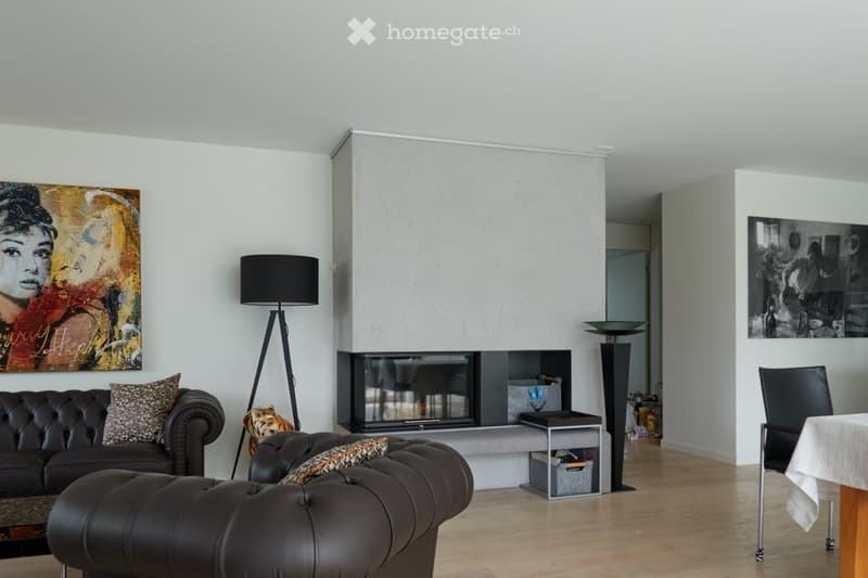 Modern living room with a dark leather sofa, ottoman, coffee table, floor lamp, fireplace, and artwork on the walls.
