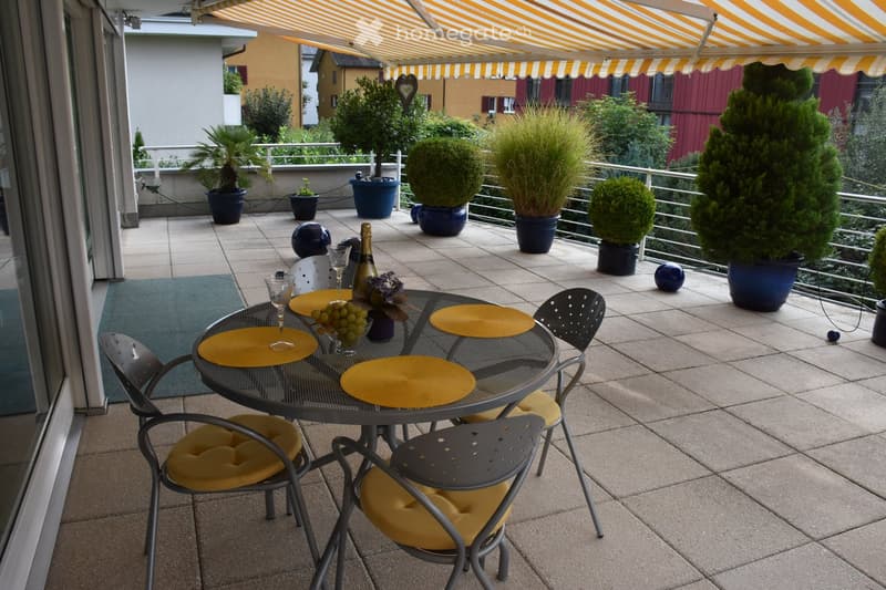 Balcony with a round metal table, four chairs, wine bottle, wine glasses, plates, and potted plants.