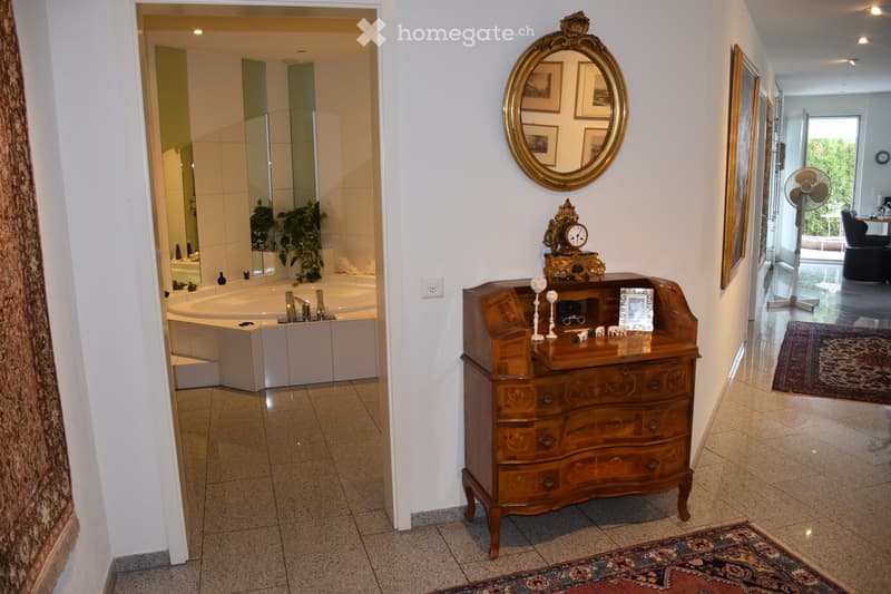Hallway with a wooden dresser, ornate mirror, and a view into a bathroom with a bathtub and sink.