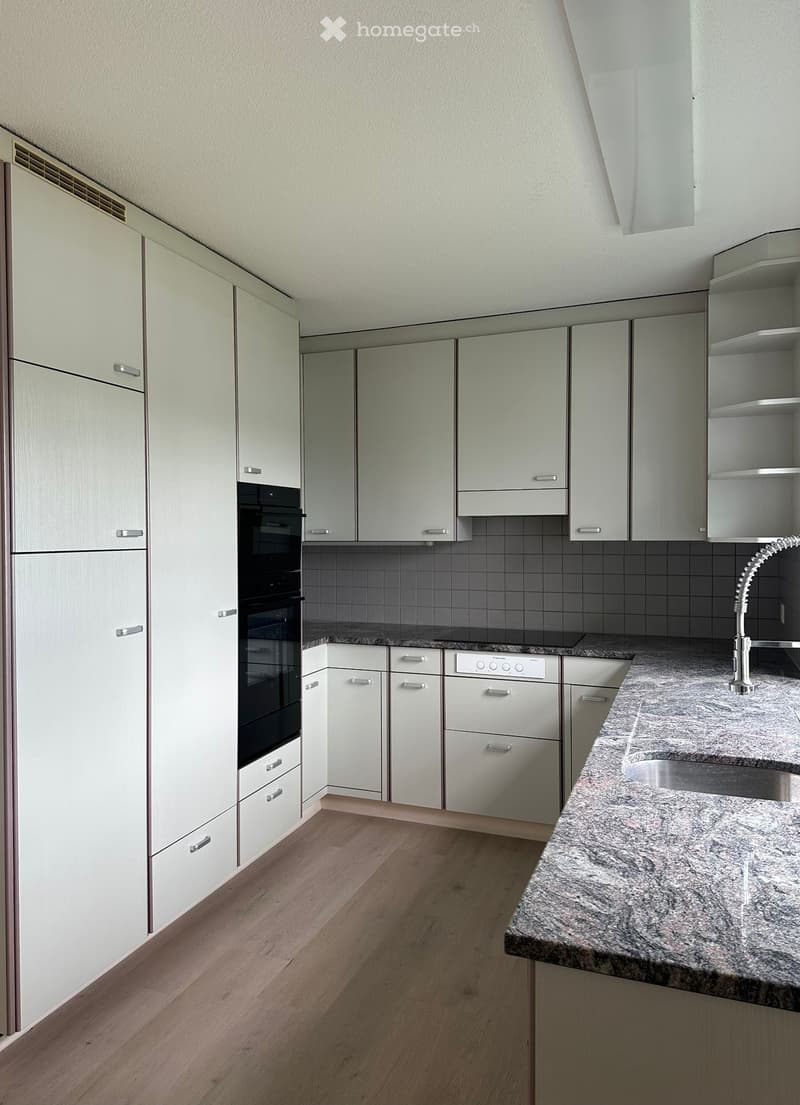 Modern kitchen with light-colored cabinets, granite countertop, stainless steel sink, and built-in oven.