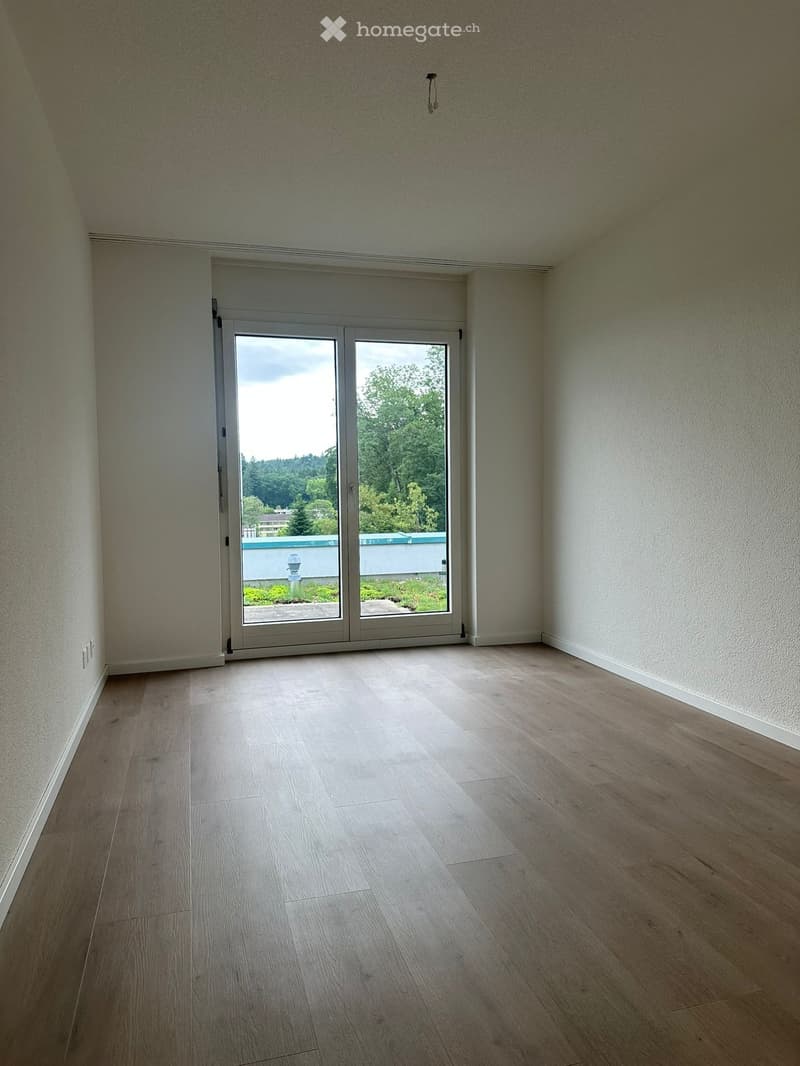 Empty room with light wooden flooring, white walls, and large sliding glass doors leading to an outdoor area.