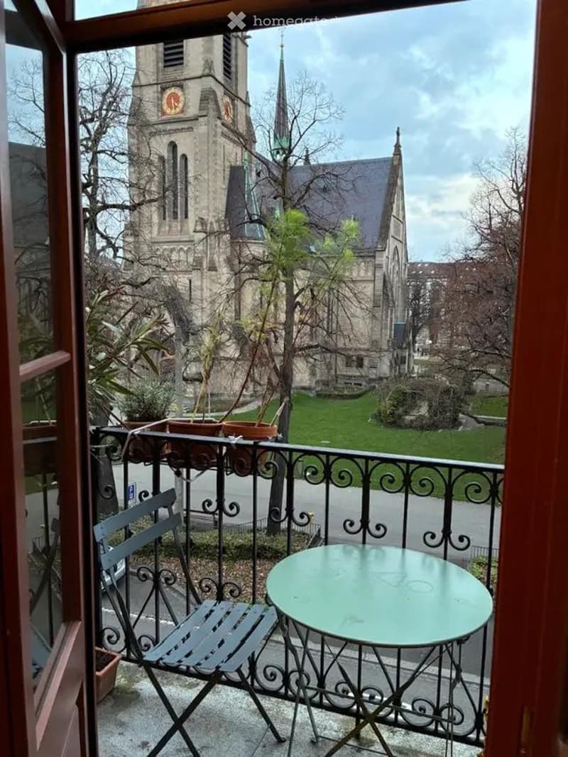 Balcony with a view of a historic church, featuring a metal chair and a round table.