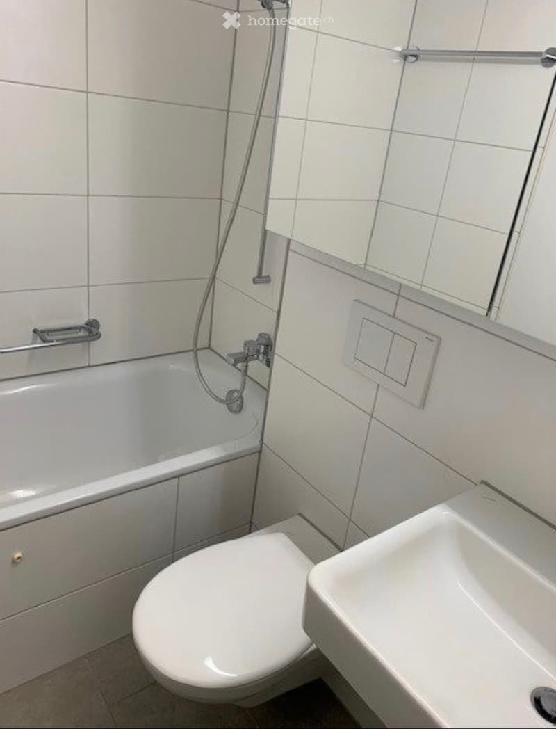 Modern bathroom with white tiled walls, a bathtub, a toilet, and a sink.