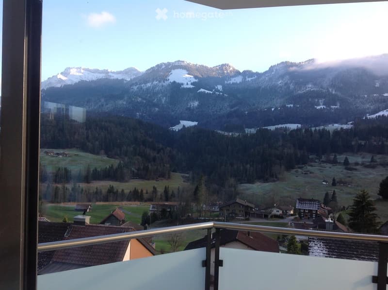 Balcony with a scenic mountain view, surrounded by forested hills and scattered houses.