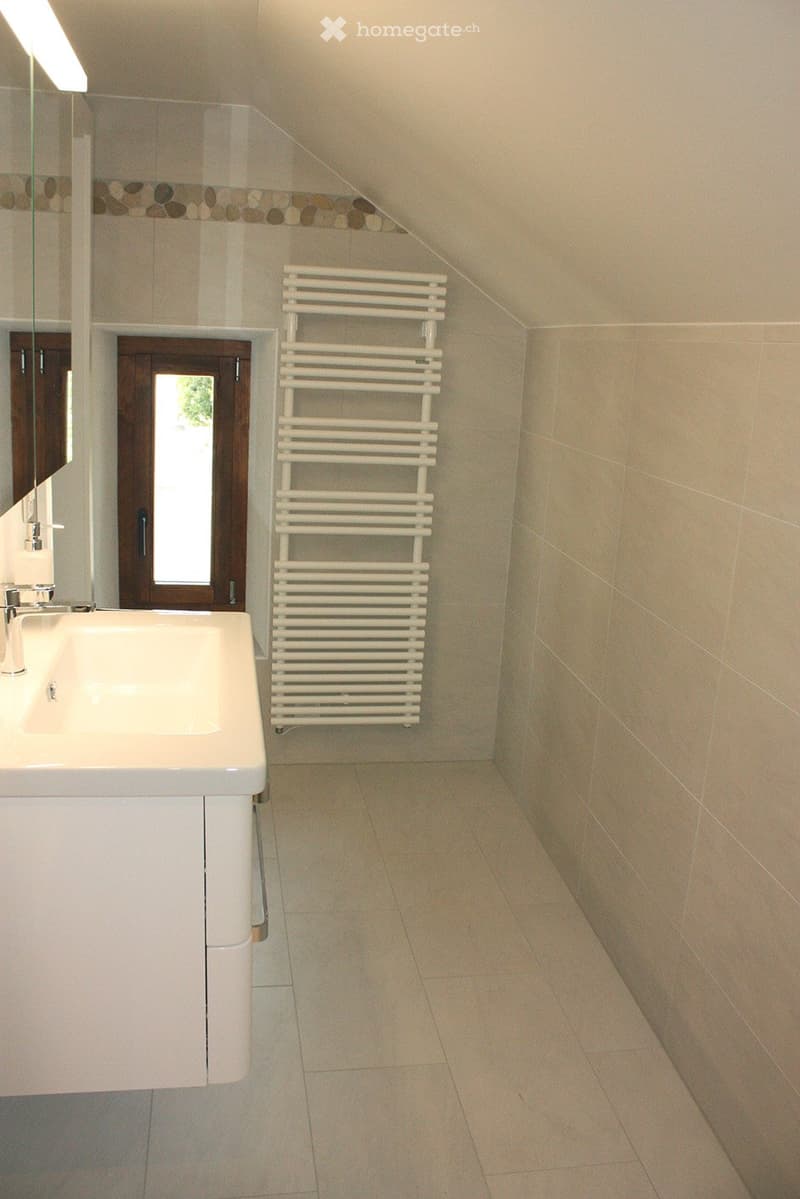 Modern bathroom with a white radiator, a sink with a modern faucet, a mirror, and a cabinet. The walls are tiled with a decorative border near the ceiling, and the floor is tiled in a light color.