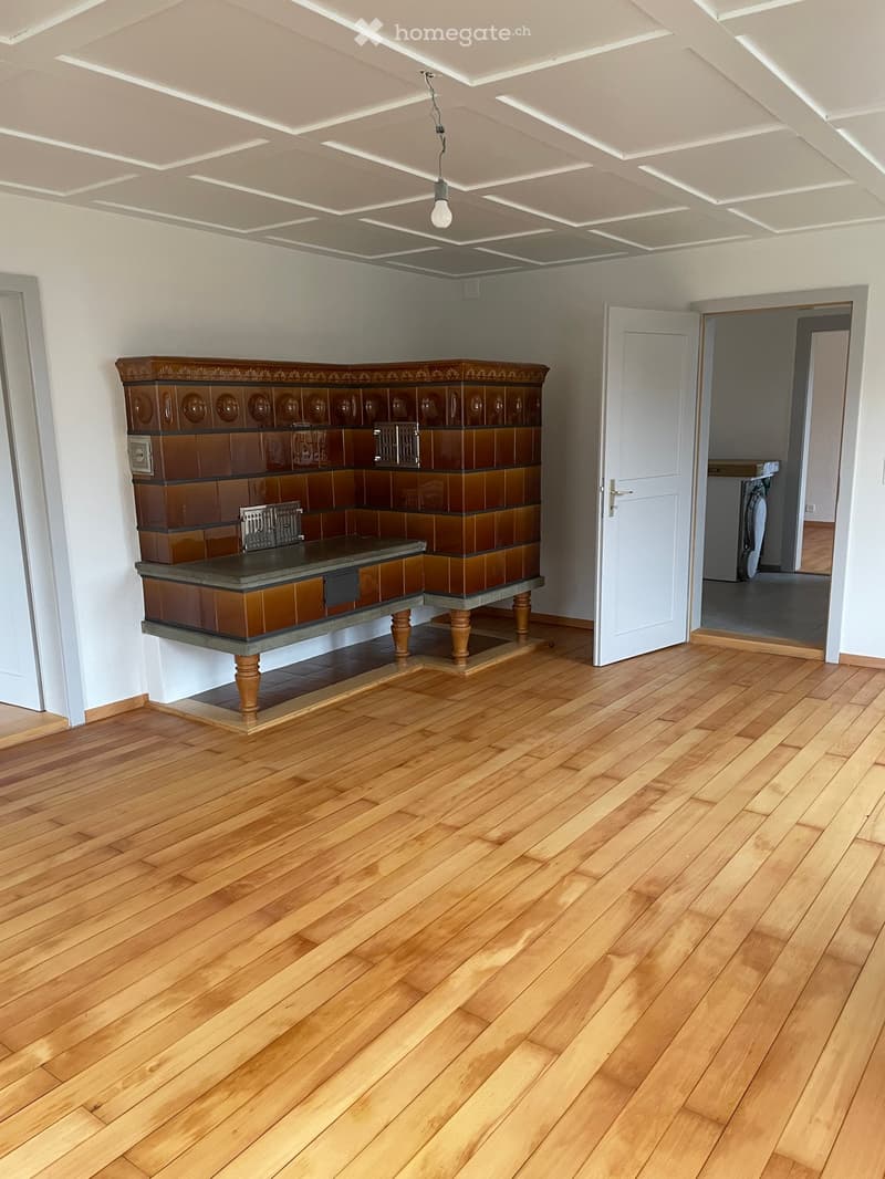 Empty room with wooden flooring, white walls, and a decorative fireplace with tiled surround. A white door is visible on the right side, leading to another room.