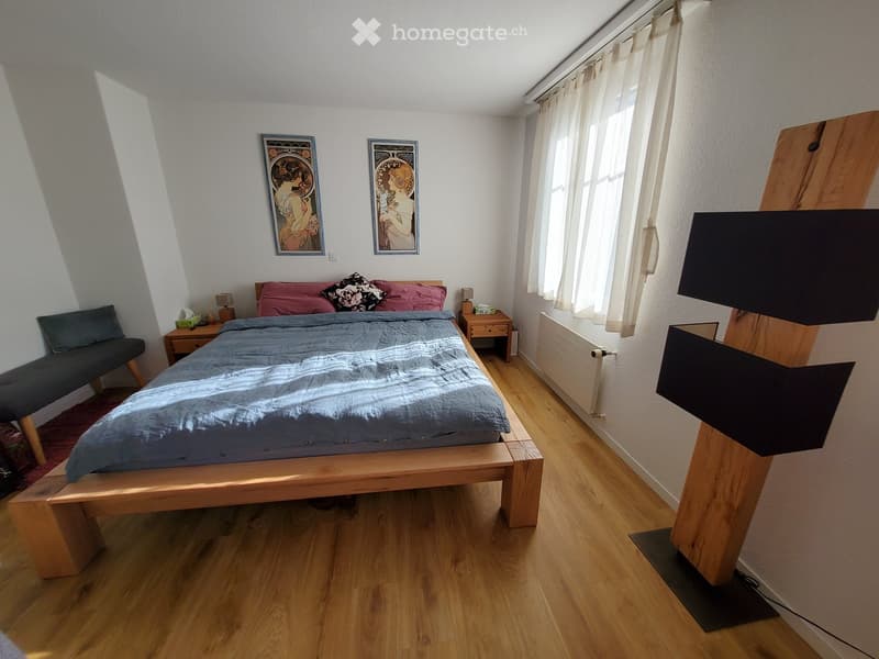Cozy bedroom with wooden flooring, a large bed with blue bedding, nightstands, a bench, and artwork on the walls.