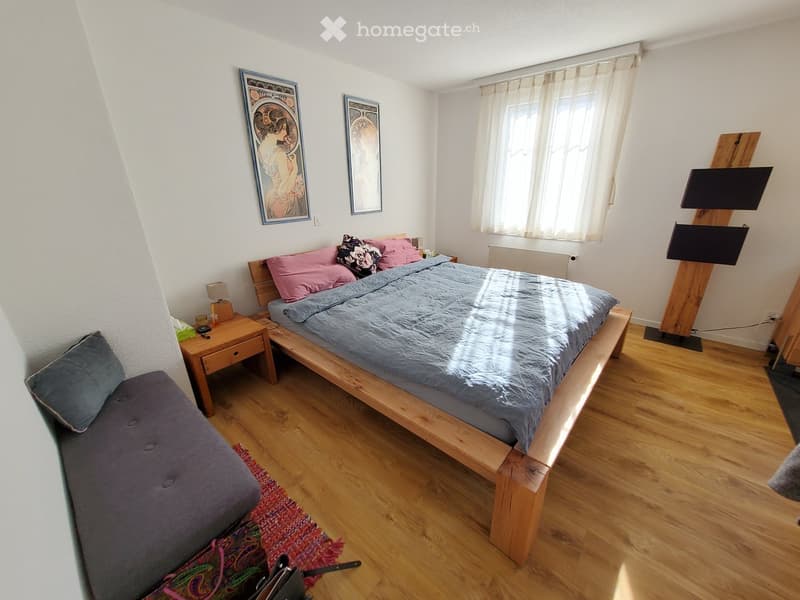Cozy bedroom with wooden bed, nightstand, sofa, and artwork on the walls.