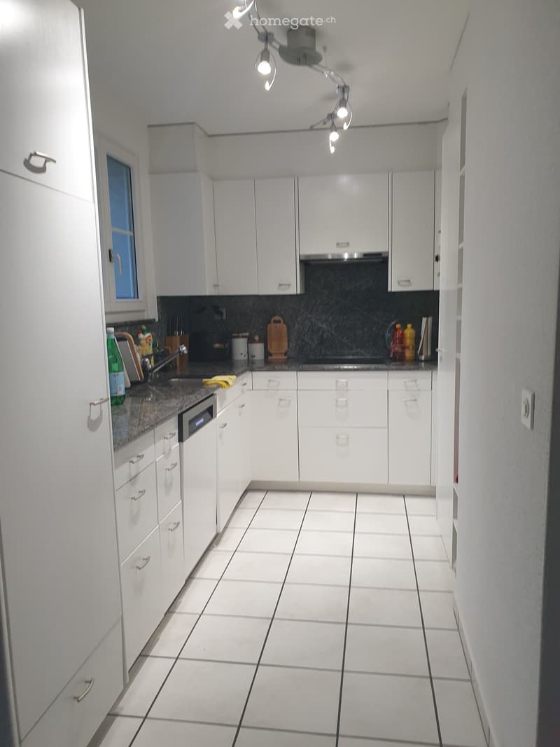 Modern kitchen with white cabinets, tiled floor, and granite countertop. Features an oven, dishwasher, and various kitchen items on the counter.