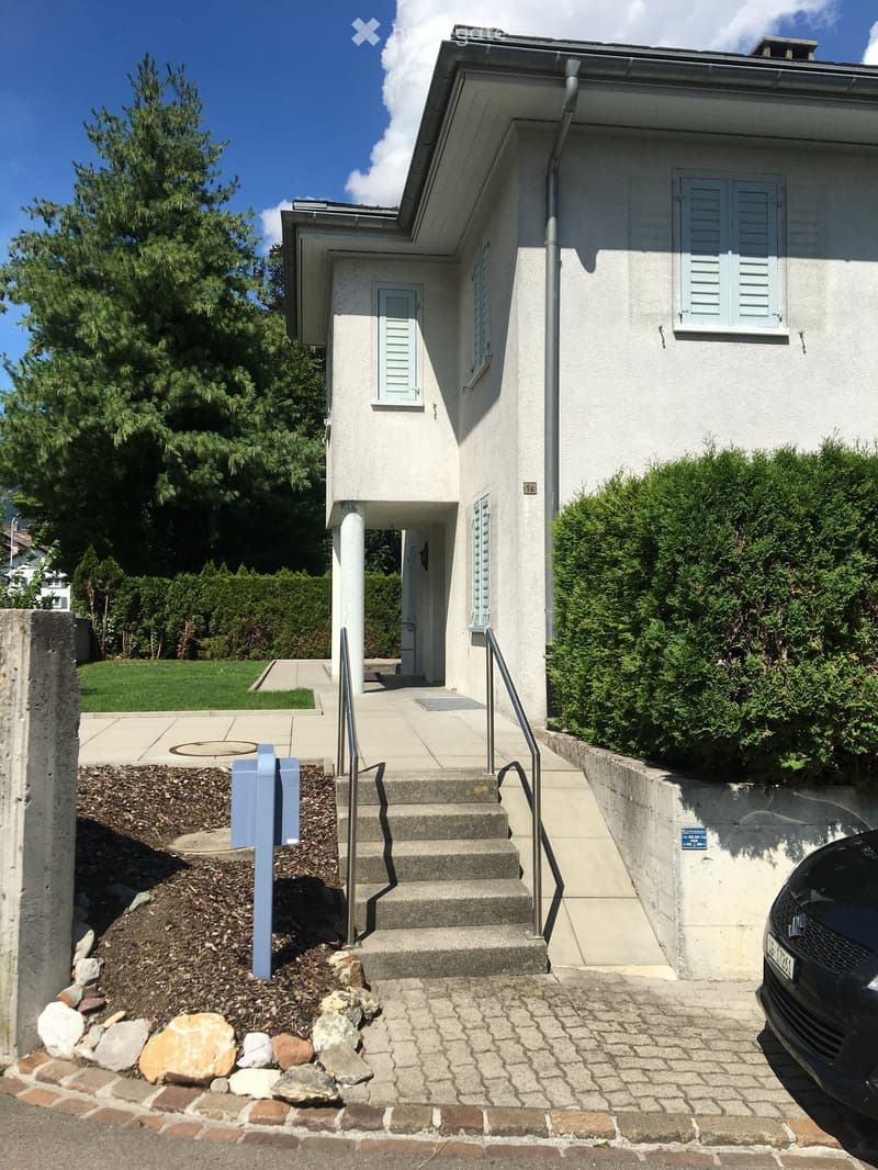 Two-story house with light-colored exterior, raised ground floor, and a small staircase leading to the entrance.