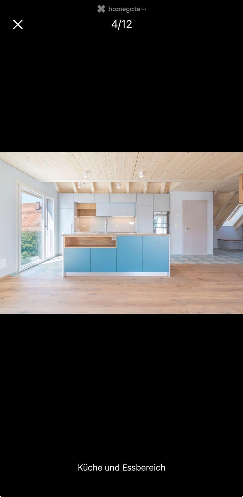 Modern kitchen with light blue cabinets, wooden countertop, and stainless steel appliances. Large windows provide natural light.